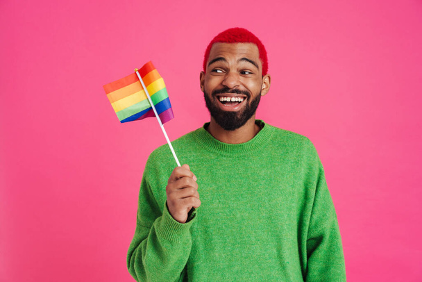 Joyful african american guy laughing and holding rainbow flag isolated over pink background - Foto, Imagem