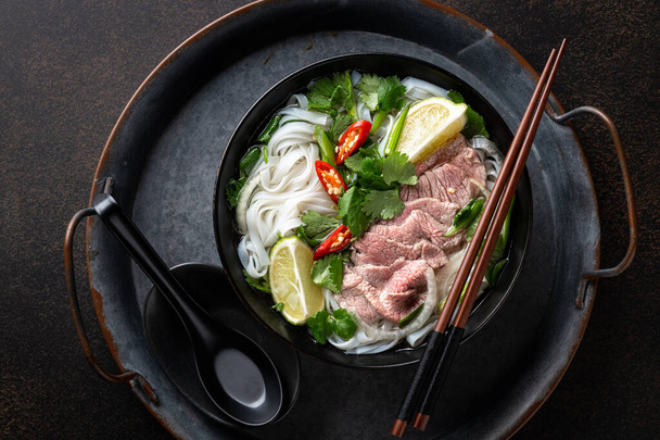 Pho Bo vietnamese soup with beef and rice noodles on a dark background, top view - Foto, Bild
