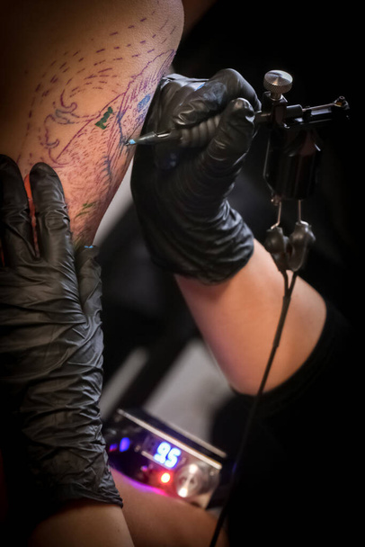 Женщина-татуировщица делает татуировку на руке мужчины
 - Фото, изображение