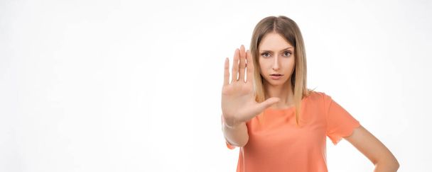 I say no. Serious blond girl keeps palm forward at camera, makes forbid sign, restricts or warns, extends arm in stop sign. Studio shot, white background. Place for ad - Photo, Image