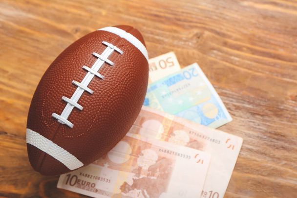 Pieniądze i rugby piłkę na drewnianym tle. Pojęcie zakładu sportowego - Zdjęcie, obraz
