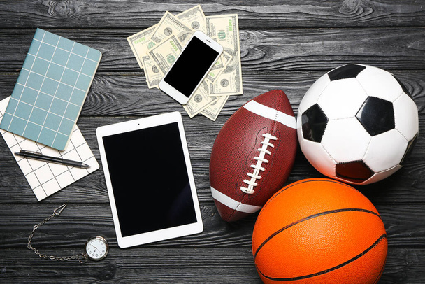 Tablet ordenador, teléfono móvil, dinero y pelotas sobre fondo de madera oscura. Concepto de apuesta deportiva - Foto, Imagen
