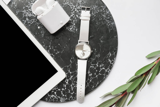 Stylish wristwatch, tablet computer and earphones on light background - Photo, Image