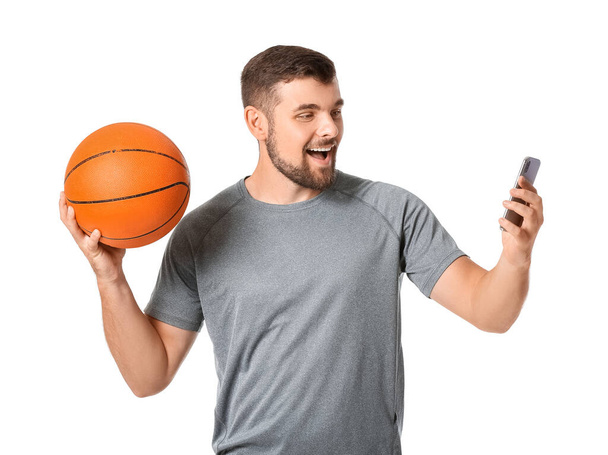 Jeune homme avec téléphone portable et balle sur fond blanc. Concept de pari sportif - Photo, image