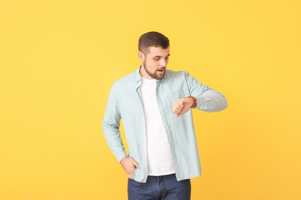 Young man looking at wristwatch on color background - Φωτογραφία, εικόνα
