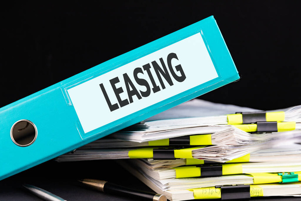 Text LEASING is written on a folder lying on a stack of papers with a pen on the table. Business concept - Photo, image