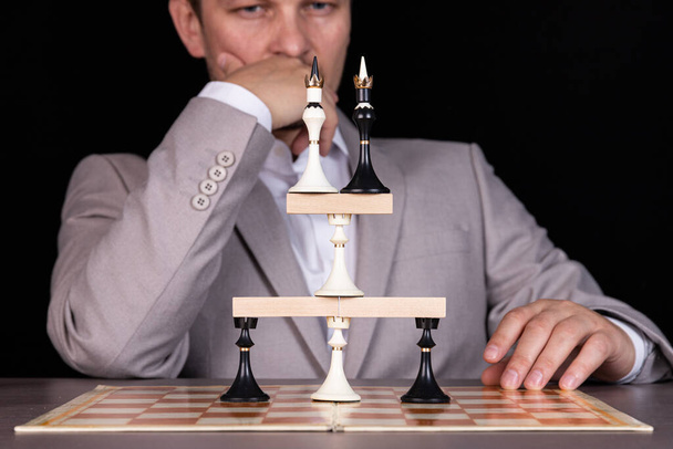 A businessman is building a pyramid of chess pieces and wooden blocks. The concept of construction, growth, development, success. - Фото, зображення