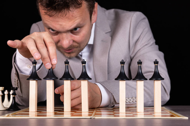 A businessman is building a pyramid of chess pieces and wooden blocks. The concept of construction, growth, development, success. - Fotografie, Obrázek