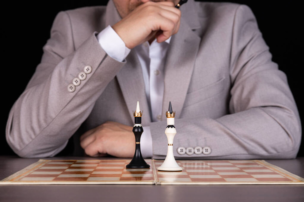 Człowiek, biznesmen siedzi przy szachownicy. Na tablicy jest czarno-biały król. Koncepcja zarządzania, dyskryminacja rasowa. - Zdjęcie, obraz