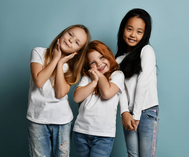 International kids girls friends in jeans and white t-shirts stand together melting feeling touched love - Foto, Imagen