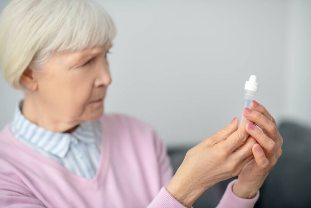Senior woman holding a bottle with eyedrops - Foto, afbeelding