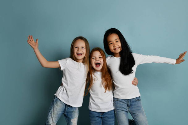 Cheerful multiracial girls friends in jeans and white t-shirts have fun together laughing playing hugging each other  - Photo, image