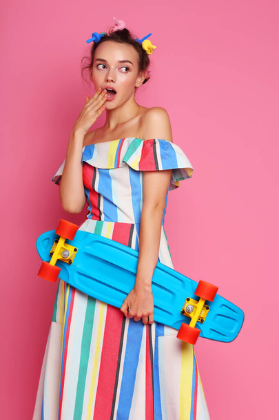 Fashion cool girl posing with a skateboard on pink background. Young hipster woman, studio shot - Foto, Imagen