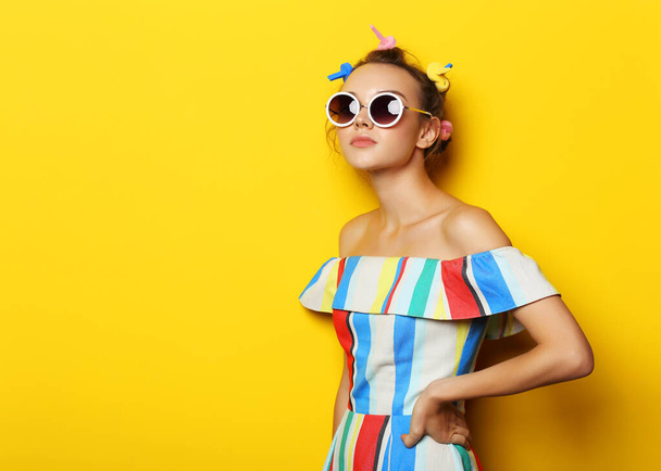 Fashion cool girl posing in sunglasses on yellow background. Young hipster woman, curlers in her hair  - Фото, зображення