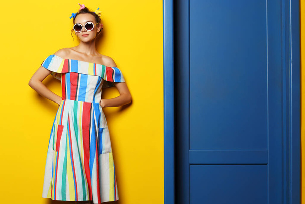 Fashion cool girl posing in sunglasses on yellow background. Young hipster woman, curlers in her hair  - Foto, immagini