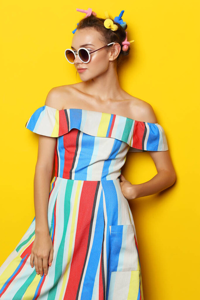 Fashion cool girl posing in sunglasses on yellow background. Young hipster woman, curlers in her hair  - Foto, Bild