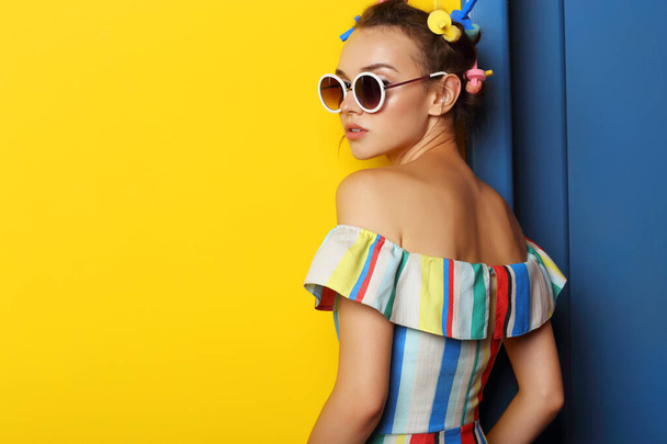 Fashion cool girl posing in sunglasses on yellow background. Young hipster woman, curlers in her hair  - Valokuva, kuva