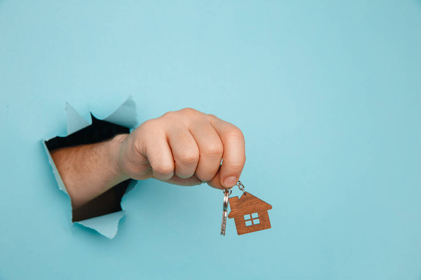 Mans mano con le chiavi di casa attraverso un buco in carta blu. Casa vendita e affitto concetto - Foto, immagini