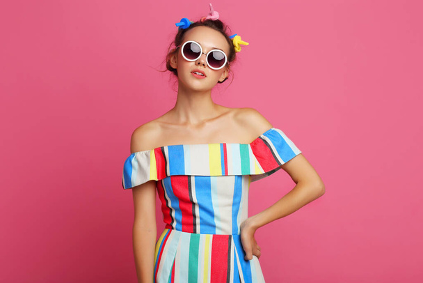 Fashion cool girl posing on pink background. Young hipster woman, curlers in her hair, sunglasses - Zdjęcie, obraz