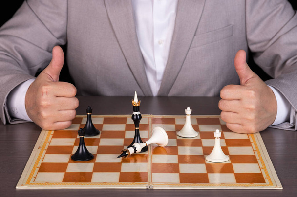 Ένας άντρας, ένας επιχειρηματίας παίζει με πιόνια του σκακιού, το ένα κομμάτι νικάει το άλλο. Η έννοια της εξουσίας, της διακυβέρνησης, του ρατσισμού. - Φωτογραφία, εικόνα
