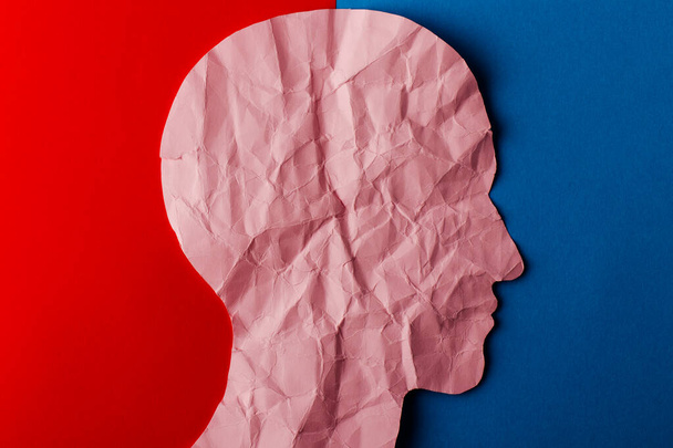 Head silhouette made of paper. Crumpled pink paper shaped as a human head with copy space on red and blue paper background. Minimal concept. - Foto, Bild