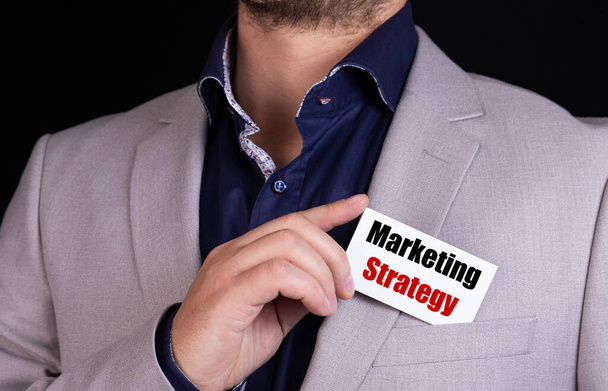 MARKETING STRATEGY text is written on the card that the businessman puts in his jacket pocket. Business concept. - Фото, изображение