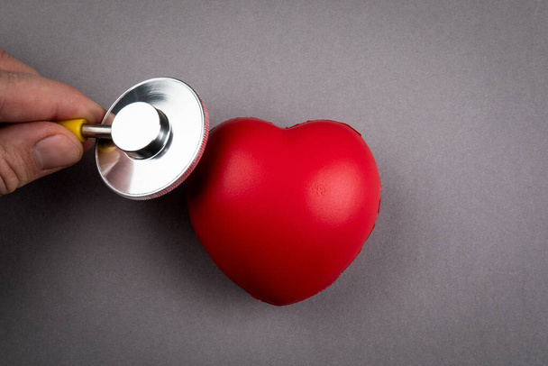 Battito cardiaco e controllo di salute. cuore di gomma rossa e stetoscopio su sfondo grigio - Foto, immagini