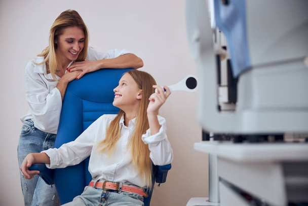 Šťastná veselá blondýna běloška matka mluví s roztomilou dcerou v kanceláři pediatrický oftalmolog - Fotografie, Obrázek