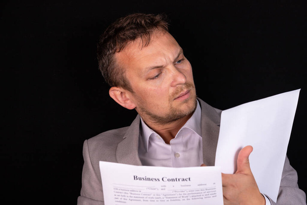 Επιχειρηματίας μελετώντας ένα έγγραφο χαρτί με μια σοβαρή έκφραση, καθώς κάθεται στο γραφείο του στο γραφείο - Φωτογραφία, εικόνα