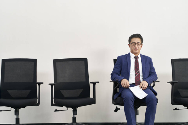 ältere asiatische Arbeitssuchende bereiten sich mit geschlossenen Augen auf ein Vorstellungsgespräch vor, während sie in der Schlange stehen - Foto, Bild