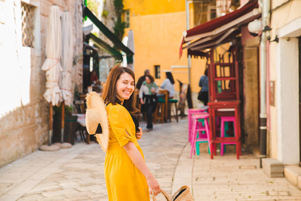 小さなクロアチアの街を歩く黄色いサンドレスの観光客の女性。夏休みのコンセプト - 写真・画像