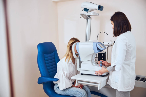 Unrecognized female in casual clothes checking her eyesight in professional ophthalmology center - Фото, изображение