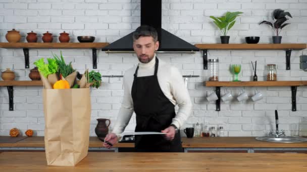 Férfi séf fekete kötény tesz kés és a fedélzeten a vágás zöldségek a konyhában - Felvétel, videó
