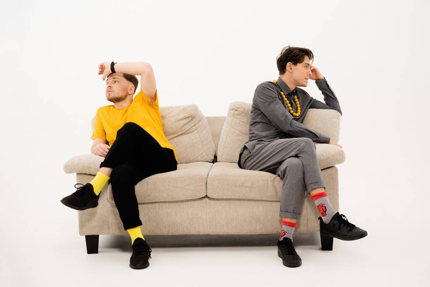 Two handsome guys had a fight while sitting on opposite sides of the sofa. Group of friends are sitting on a soft couch and communicates isolated on white background - Fotó, kép