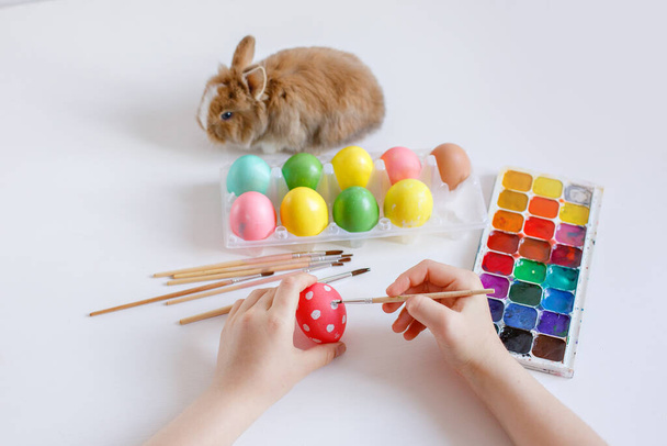 Bir çocuğun elleri beyaz arka planda bir Paskalya yumurtası süsler. - Fotoğraf, Görsel