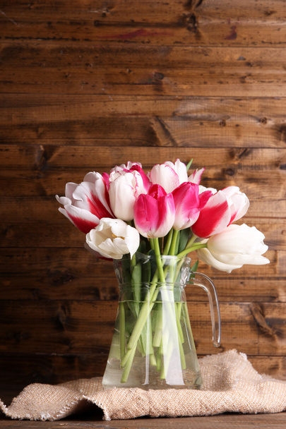 Beautiful tulips in glass jug on wooden background - Foto, imagen