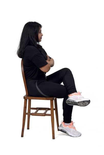 Seitenansicht einer lateinischen Frau, die auf einem Stuhl sitzt und die Beine überkreuzt, weißer Hintergrund, - Foto, Bild