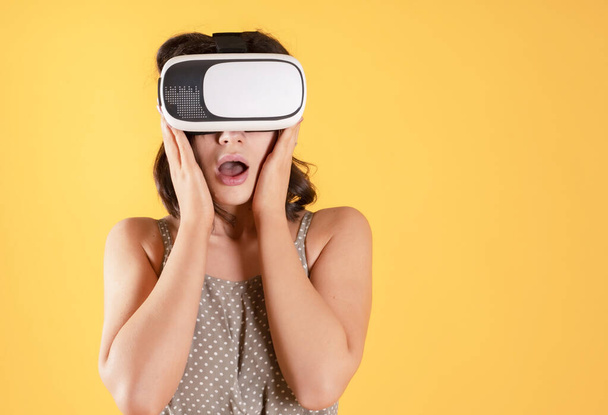 brunette woman in casual clothes wearing virtual reality glasses playing happy on yellow background - Foto, Imagen