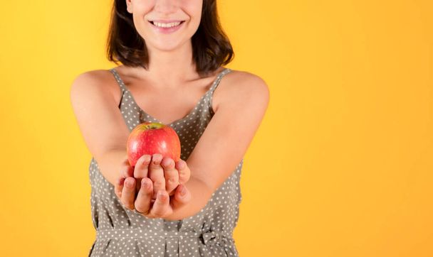 pretty woman with black hair, casual clothes, holding an apple, healthy food concept, yellow background - Foto, imagen