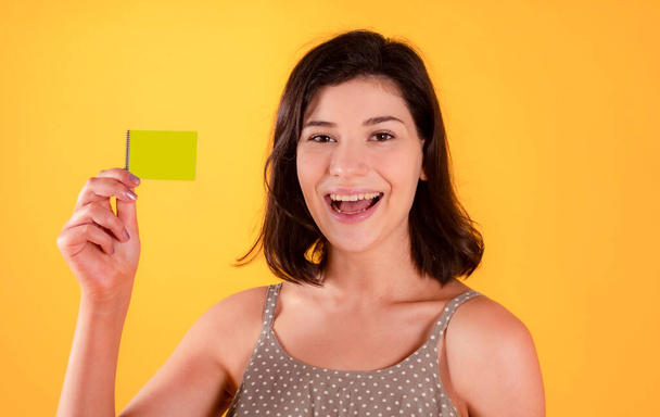 pretty brunette woman in casual clothes, happy uses her credit card, on yellow background - Foto, Bild