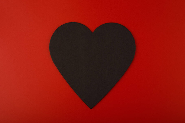 Close up of black paper heart against red background with copy space. Minimalistic concept of Valentines day  - Foto, immagini