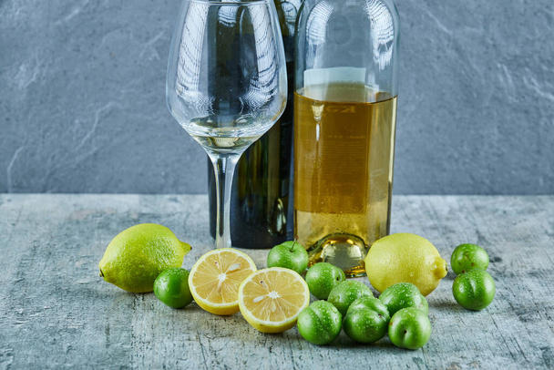 Kaksi pulloa ja lasi viiniä marmoripöydällä sitruunoilla ja kirsikkaluumuilla - Valokuva, kuva