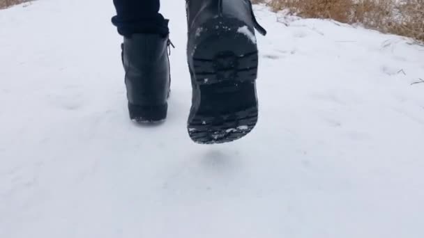 Pieds enfantins en chaussures noires gros plan marchant sur la neige blanche. La fille marche à travers la neige sous laquelle vous pouvez voir l'herbe sèche. - Séquence, vidéo