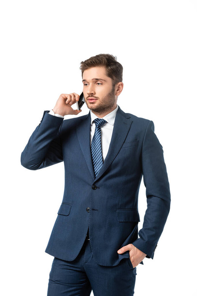 joven hombre de negocios con la mano en el bolsillo hablando en el teléfono móvil aislado en blanco - Foto, imagen
