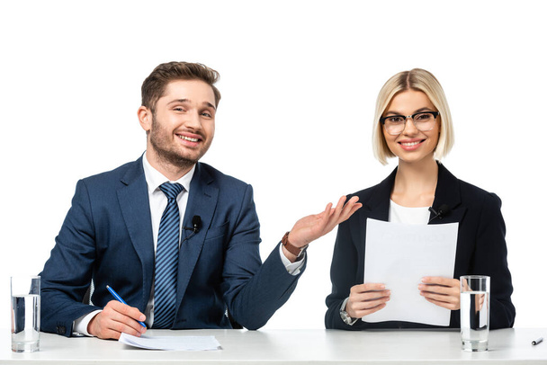 heureux présentateur de nouvelles pointant vers un collègue souriant tenant du papier sur le lieu de travail isolé sur blanc - Photo, image