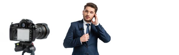 news presenter fixing earphone near digital camera on blurred foreground isolated on white, banner - Photo, Image