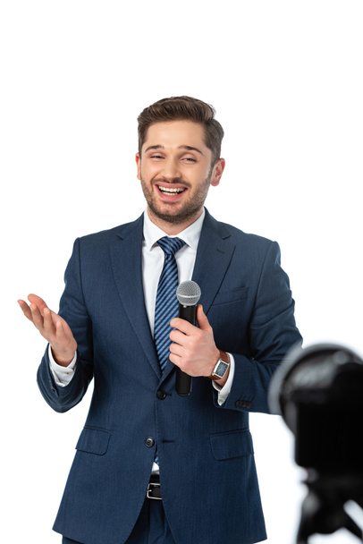 χαμογελαστός δημοσιογράφος με μικρόφωνο δείχνοντας με το χέρι απομονωμένο σε λευκό, θολό προσκήνιο - Φωτογραφία, εικόνα