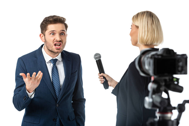 periodista rubia entrevistando hombre de negocios enojado cerca de la cámara digital en primer plano borroso aislado en blanco - Foto, Imagen