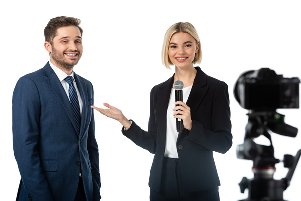 uśmiechnięta prezenterka wiadomości wskazująca szczęśliwego biznesmena podczas wywiadu przy aparacie cyfrowym odizolowanym na białym, niewyraźnym pierwszym planie - Zdjęcie, obraz
