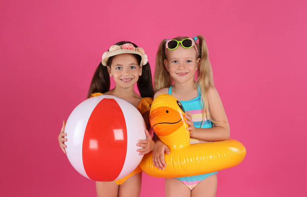 Cute little children in beachwear with bright inflatable toys on pink background - Valokuva, kuva